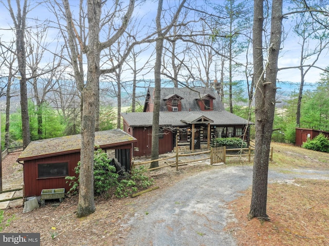 rustic home featuring driveway, a chimney, and roof with shingles