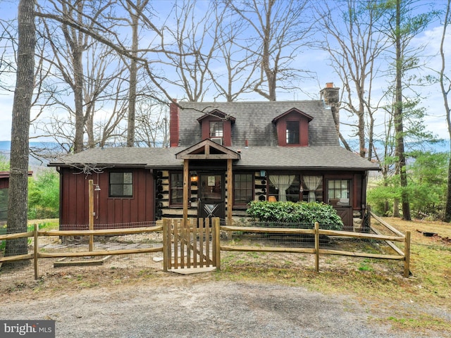 chalet / cabin featuring a chimney, a shingled roof, board and batten siding, and a fenced front yard