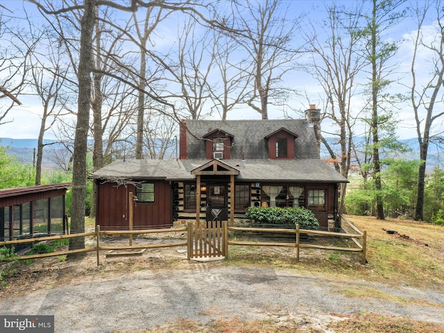chalet / cabin with a gate, roof with shingles, a chimney, board and batten siding, and a fenced front yard