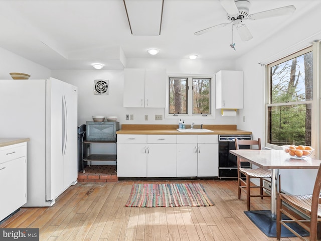 kitchen with white cabinetry, light countertops, light wood-type flooring, dishwasher, and freestanding refrigerator
