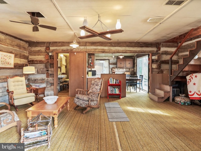 unfurnished living room featuring log walls, stairway, ceiling fan, and visible vents