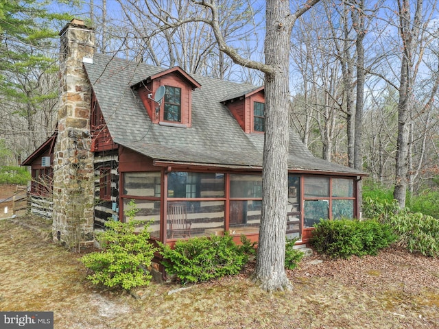 view of front facade with a sunroom, a shingled roof, and a chimney