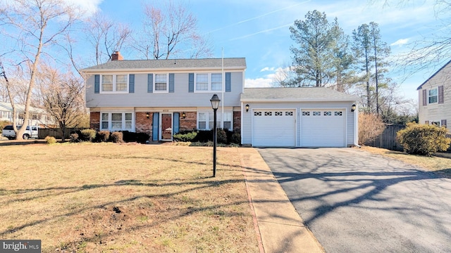 colonial house with brick siding, a chimney, aphalt driveway, an attached garage, and a front yard