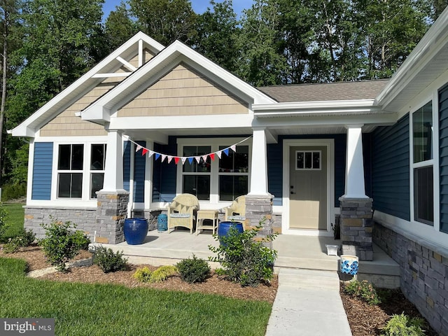 entrance to property featuring stone siding, a porch, and roof with shingles