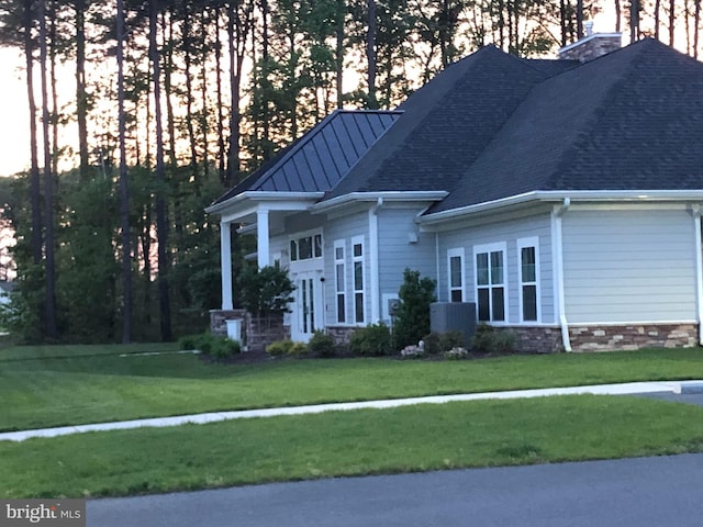 view of front facade with a shingled roof, central AC unit, a chimney, a standing seam roof, and a front lawn