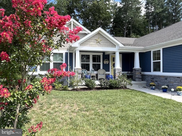 view of front of property with stone siding, a porch, roof with shingles, and a front yard