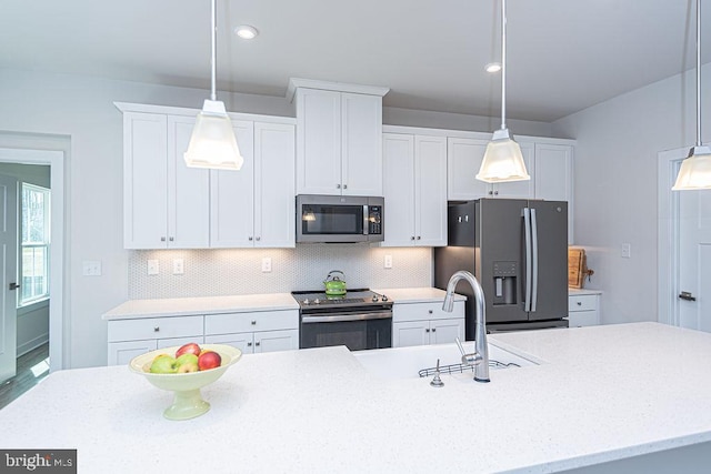 kitchen with appliances with stainless steel finishes, decorative light fixtures, a sink, white cabinetry, and backsplash