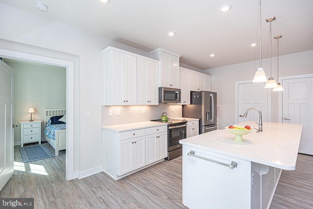 kitchen with a center island with sink, light wood-style flooring, backsplash, appliances with stainless steel finishes, and white cabinetry