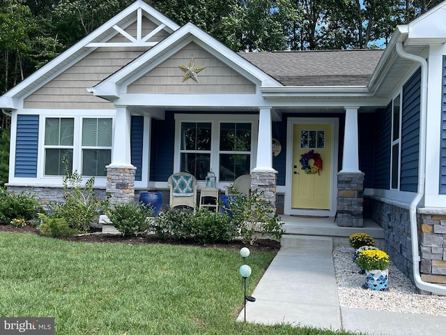 property entrance with a yard, stone siding, a porch, and roof with shingles