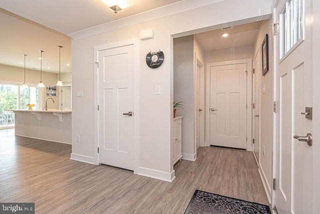 hallway with a sink, baseboards, wood finished floors, and recessed lighting