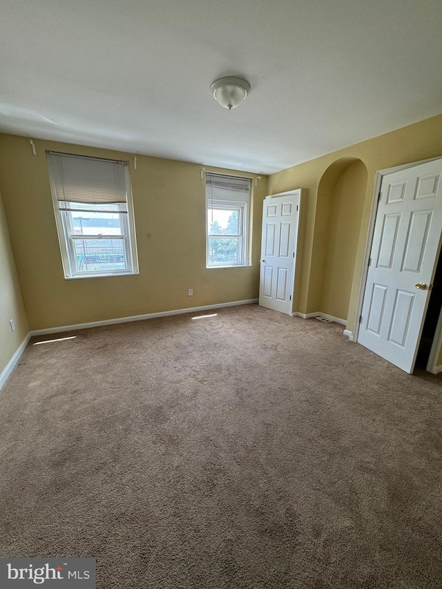 unfurnished bedroom featuring arched walkways, baseboards, and carpet