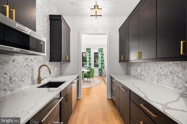 kitchen with light wood-style flooring, dark cabinets, a sink, stainless steel appliances, and backsplash