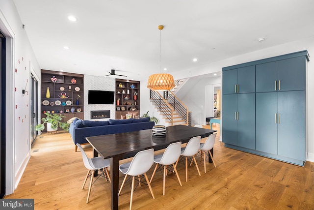 dining area with light wood-type flooring, built in shelves, stairs, and a tiled fireplace