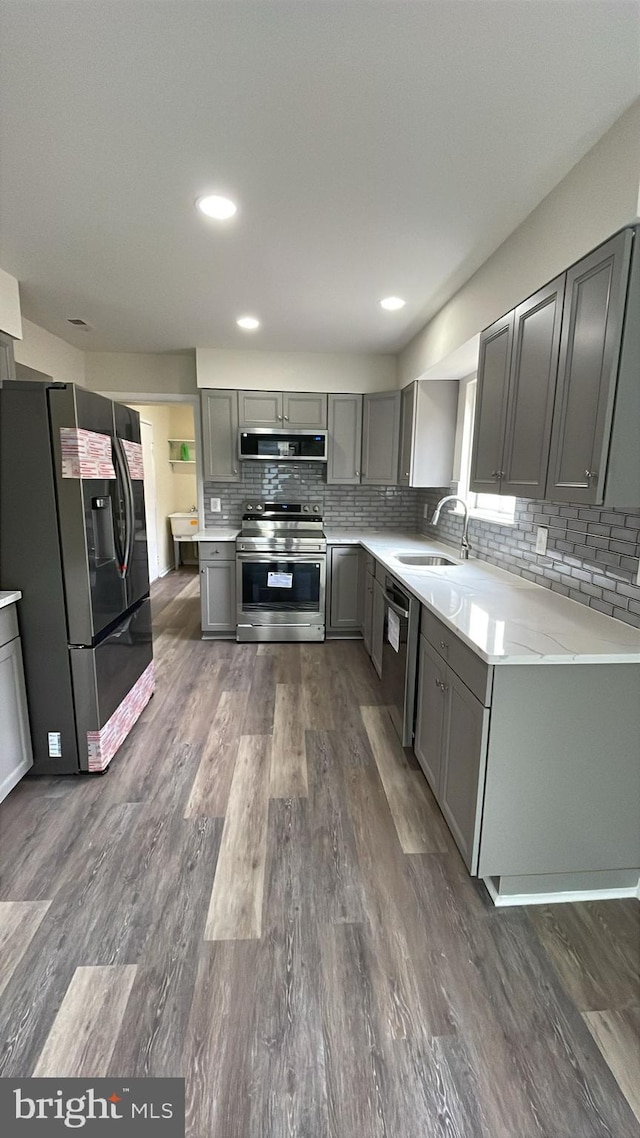 kitchen featuring appliances with stainless steel finishes, gray cabinets, a sink, and tasteful backsplash