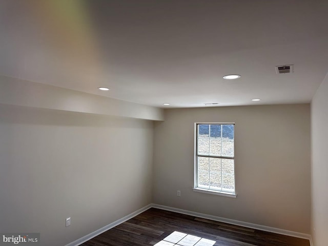 empty room with dark wood-style floors, recessed lighting, visible vents, and baseboards