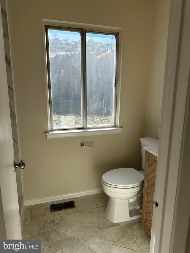 half bathroom featuring toilet, marble finish floor, baseboards, and visible vents