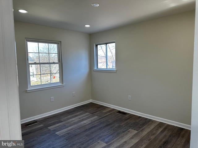 spare room with dark wood-style flooring, visible vents, and baseboards