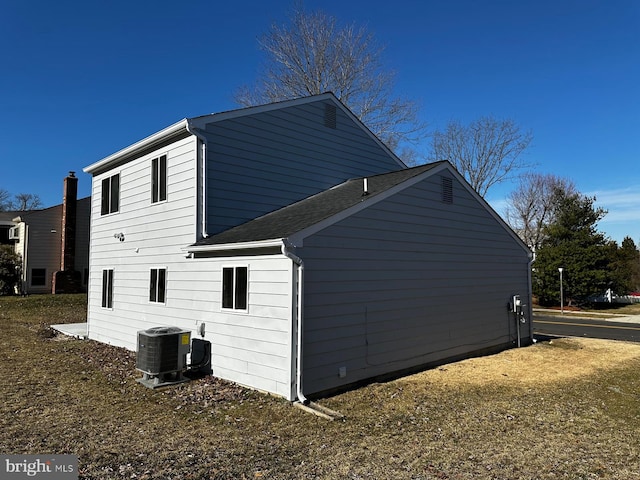 view of side of home featuring a shingled roof and central AC