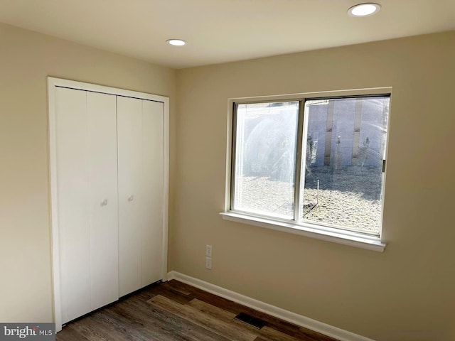 unfurnished bedroom with dark wood-type flooring, a closet, multiple windows, and visible vents