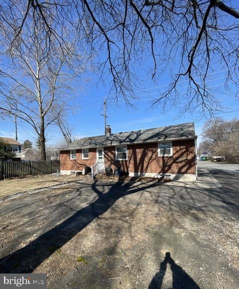 view of front facade featuring driveway, brick siding, a chimney, and fence