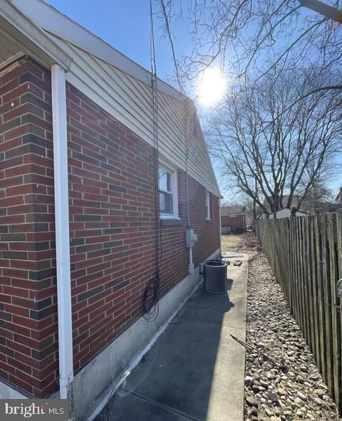 view of side of home featuring fence, cooling unit, and brick siding