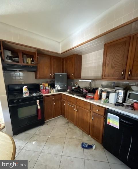 kitchen featuring light tile patterned floors, brown cabinets, under cabinet range hood, light countertops, and black appliances