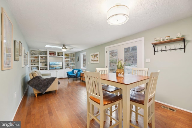 dining area with baseboards, a textured ceiling, visible vents, and wood finished floors