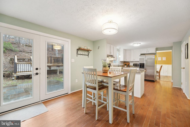 dining space featuring light wood-style floors, french doors, a textured ceiling, and baseboards