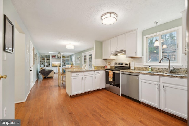 kitchen featuring stainless steel appliances, open floor plan, a sink, a peninsula, and under cabinet range hood