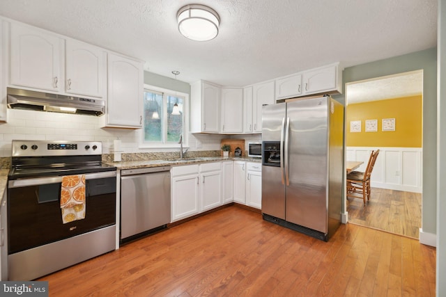 kitchen featuring stainless steel appliances, light stone countertops, white cabinetry, and under cabinet range hood