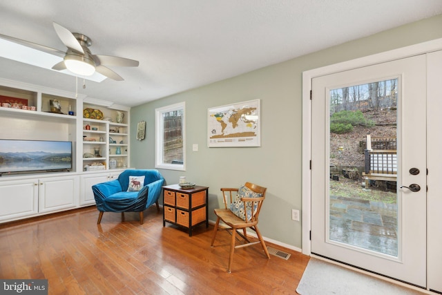 living area with ceiling fan, hardwood / wood-style flooring, a wealth of natural light, and baseboards