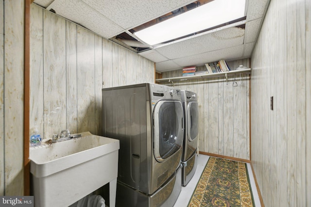 clothes washing area with laundry area, wooden walls, separate washer and dryer, and a sink