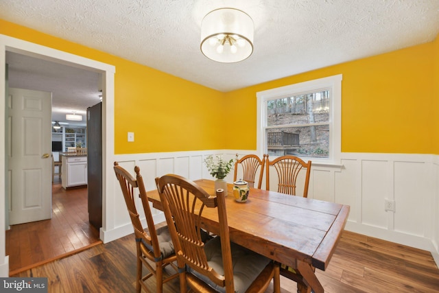 dining area featuring dark wood-type flooring, wainscoting, and a textured ceiling