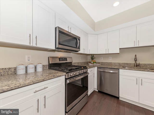 kitchen with dark wood-style flooring, appliances with stainless steel finishes, white cabinets, a sink, and light stone countertops