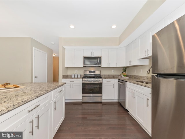 kitchen featuring dark wood-style flooring, a sink, white cabinetry, appliances with stainless steel finishes, and light stone countertops