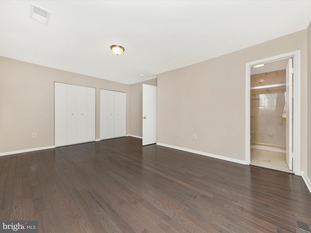 unfurnished bedroom featuring visible vents, dark wood finished floors, baseboards, and two closets