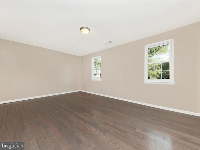 empty room with dark wood-style floors, visible vents, and baseboards