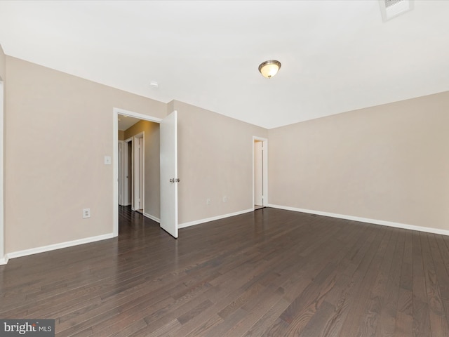 empty room featuring dark wood-style flooring, visible vents, and baseboards