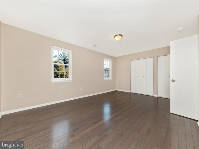 unfurnished bedroom with multiple closets, dark wood-style flooring, visible vents, and baseboards