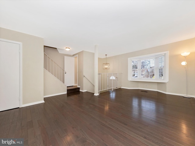 unfurnished living room featuring stairway, baseboards, wood finished floors, and an inviting chandelier