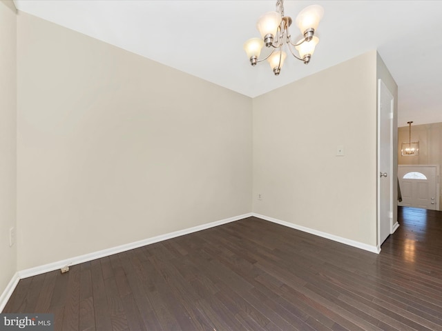 unfurnished room featuring dark wood-style floors, a notable chandelier, and baseboards