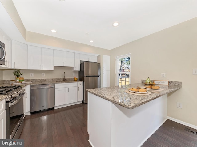 kitchen with a peninsula, a sink, white cabinetry, appliances with stainless steel finishes, and dark wood finished floors