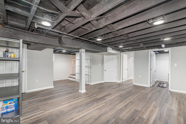 finished basement featuring stairway, wood finished floors, concrete block wall, and baseboards