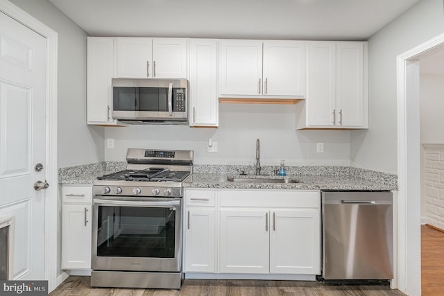 kitchen featuring appliances with stainless steel finishes, a sink, light stone countertops, and white cabinets