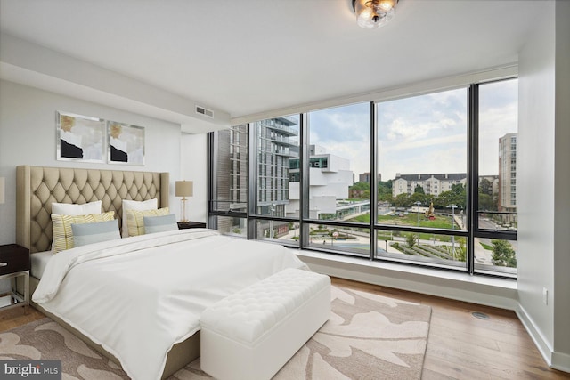 bedroom featuring a view of city, wood finished floors, visible vents, and baseboards