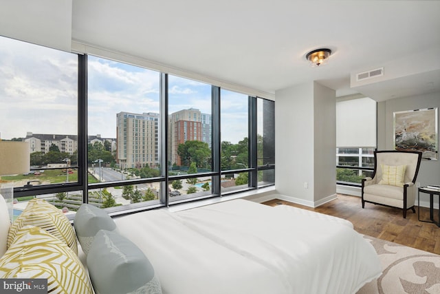 bedroom with a view of city, floor to ceiling windows, visible vents, wood finished floors, and baseboards