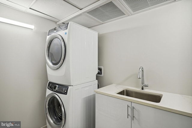 laundry room featuring stacked washer and dryer, cabinet space, visible vents, and a sink