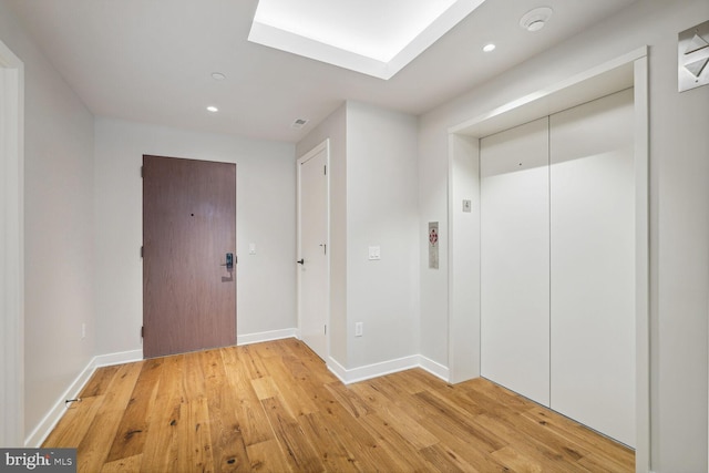 corridor with recessed lighting, a skylight, baseboards, light wood finished floors, and elevator