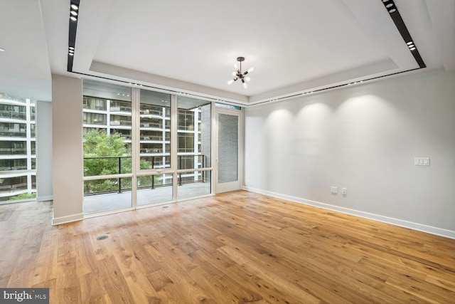 empty room featuring a tray ceiling, wood-type flooring, and baseboards