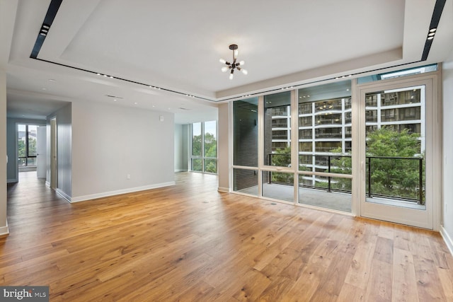 empty room with light wood-type flooring, plenty of natural light, a tray ceiling, and a notable chandelier